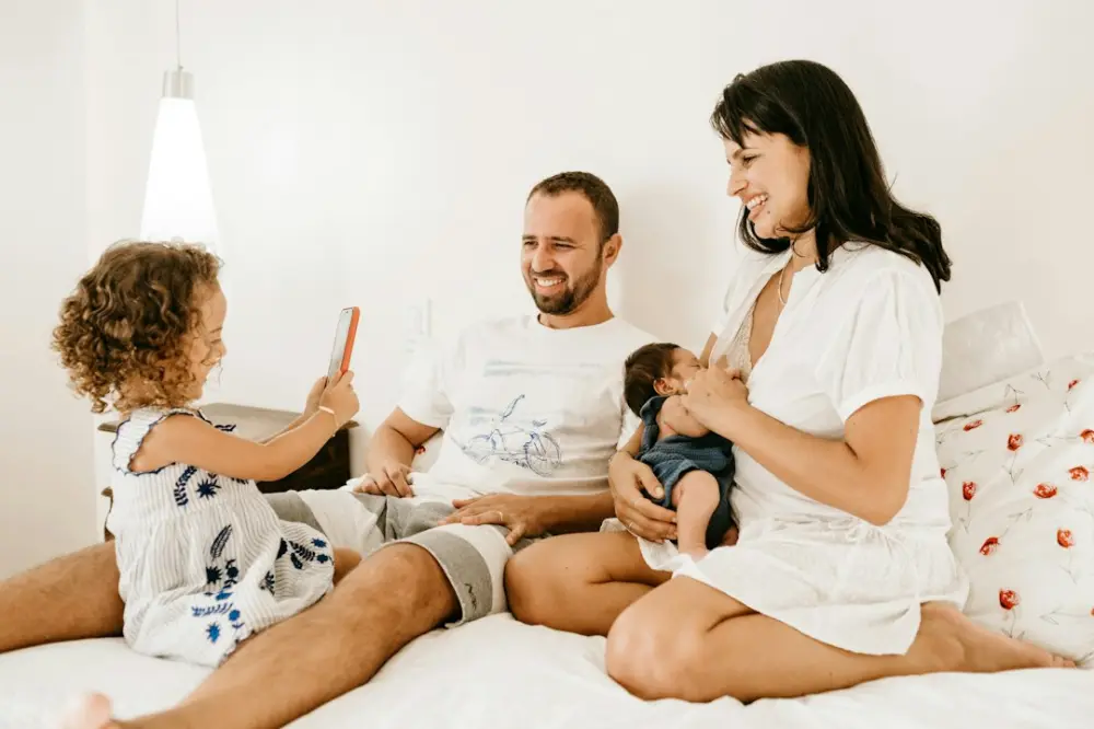 A family on a bed, a child holding a phone, an adult holding a baby, illustrating family communication